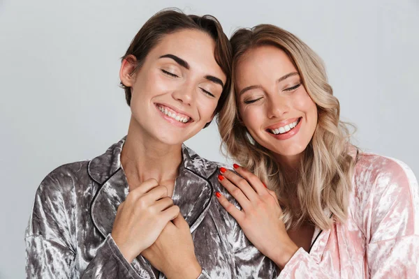 Gri arka plan üzerinde izole duran pijama giyen iki neşeli kız