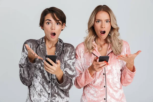 Two Pretty Shocked Girls Wearing Pajamas Isolated Gray Background Holding — ストック写真