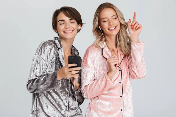 Duas Meninas Bonitas Vestindo Pijama Isolado Sobre Fundo Cinza Ouvindo — Fotografia de Stock