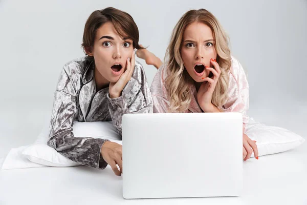Дві Шоковані Дівчата Піжамі Ізольовані Сірому Фоні Лежачи Ноутбуком — стокове фото