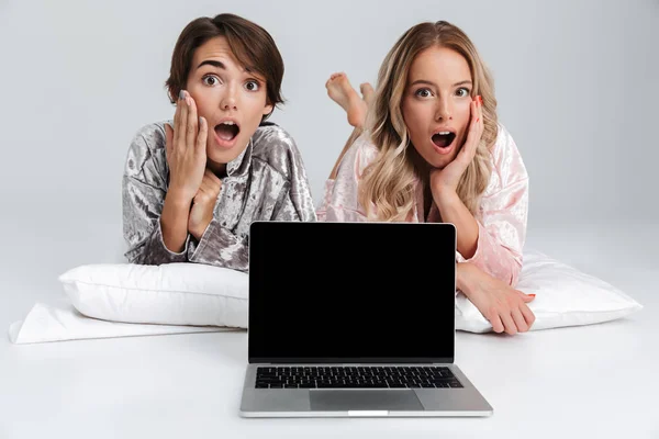 Дві Шоковані Дівчата Піжамі Ізольовані Сірому Фоні Лежачи Ноутбуком — стокове фото