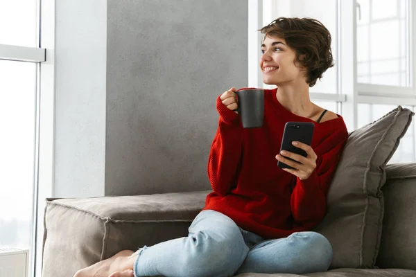 Smiling Young Woman Wearing Sweater Relaxing Couch Home Drinking Coffee — Stock Fotó