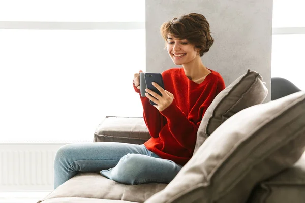 Mujer Joven Sonriente Usando Suéter Relajándose Sofá Casa Bebiendo Café — Foto de Stock