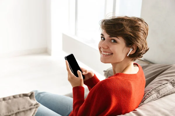 Adorável Jovem Mulher Vestindo Suéter Sentado Sofá Casa Usando Telefone — Fotografia de Stock
