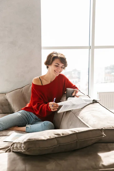 陽気な女の子がソファの上に敷設とお茶を飲みながら自宅で勉強 — ストック写真