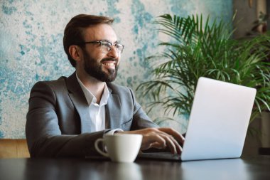 Mutlu işadamı kafede oturan ve içme kahve kapalı dizüstü bilgisayar üzerinde çalışan