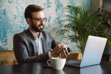 Mutlu işadamı kafede oturan ve içme kahve kapalı dizüstü bilgisayar üzerinde çalışan