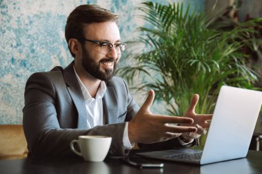 Mutlu işadamı kafede oturan ve içme kahve kapalı dizüstü bilgisayar üzerinde çalışan
