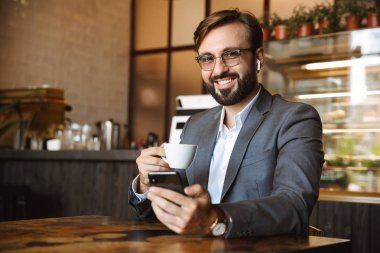Mutlu işadamı kafeterya masada otururken kahve içme cep telefonu tutan