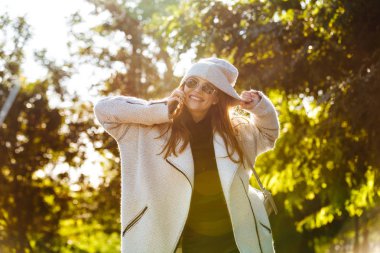 Güzel ve genç birbayan sonbahar ceket ve açık havada yürüyüş, cep telefonundan konuşuyor, gülüyor şapka giymiş