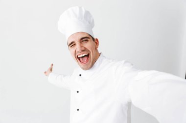 Bir selfie alarak giyen üniforma ayakta beyaz arka plan üzerinde izole mutlu Şef aşçı