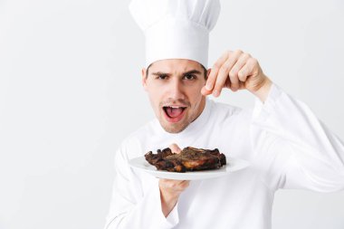 Pişmiş sığır eti biftek yemek beyaz arka plan üzerinde izole bir plaka üzerinde üniforması neşeli Şef aşçı biber