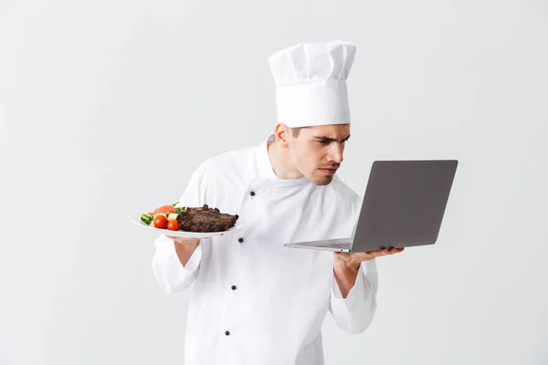 Cozinheiro Chef Sério Vestindo Uniforme Sobre Fundo Branco Segurando Computador — Fotografia de Stock