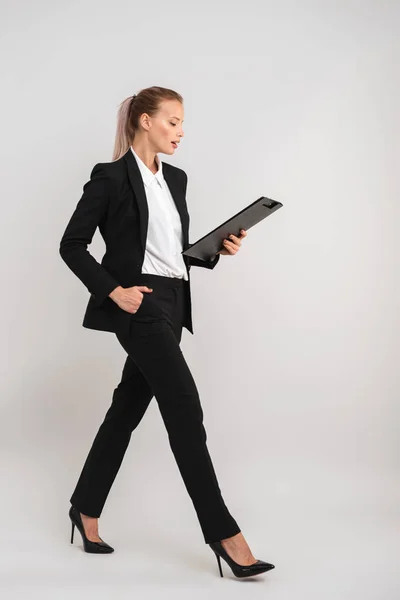 歩いてタブレットを保持している灰色の背景上分離された自信を持って若いビジネスの女性の完全な長さ — ストック写真
