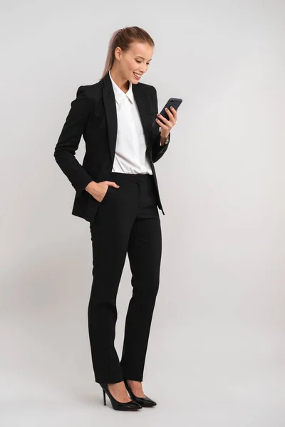 携帯電話を使用して灰色の背景上分離された笑顔の若いビジネス女性 — ストック写真