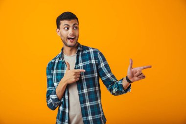 Kopya alanı, parmak işaret ekose gömlek turuncu arka plan üzerinde izole ayakta neşeli genç adam