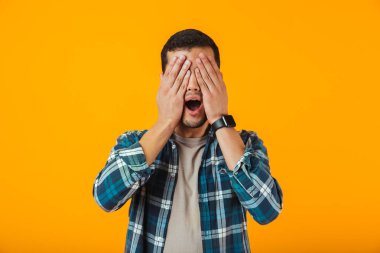 Turuncu arka plan üzerinde izole ayakta ekose gömlek giymiş şok genç adam kapak yüzü