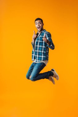 Tam uzunlukta kutluyor başarı atlama turuncu arka plan üzerinde izole ekose gömlek giymiş mutlu bir genç adam portresi