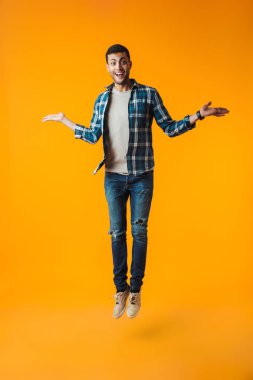 Turuncu arka plan üzerinde izole ekose gömlek giymiş mutlu bir genç adam portresi tam uzunlukta kutluyor