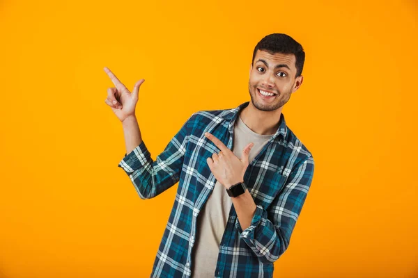 指を指している格子縞のシャツの立っているオレンジ色の背景に分離された身に着けている陽気な若い男 — ストック写真