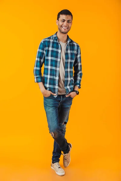 オレンジ色の背景に分離された格子縞のシャツを着て幸せな若い男の完全な長さの肖像画 — ストック写真