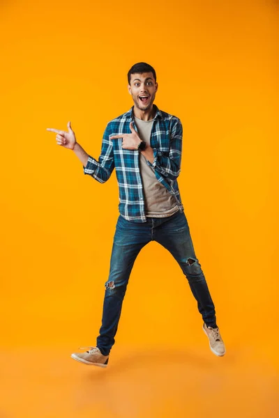 幸せな若い男のウォーキング オレンジ色の背景に分離された格子縞のシャツを着てさして全長肖像画 — ストック写真