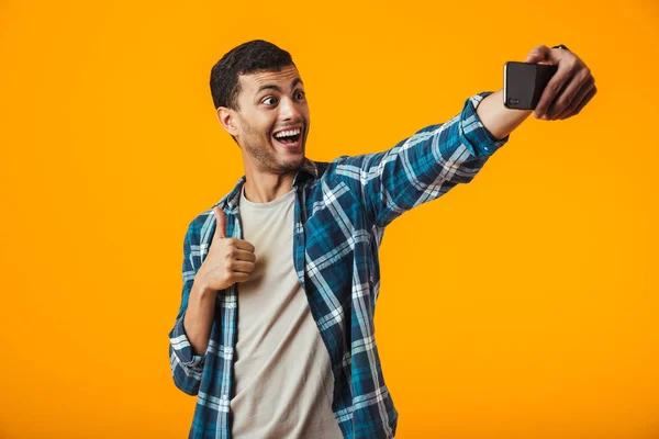 Selfie を取って 若い男を陽気なオレンジ色の背景に分離された格子縞のシャツに立って身に着けています — ストック写真
