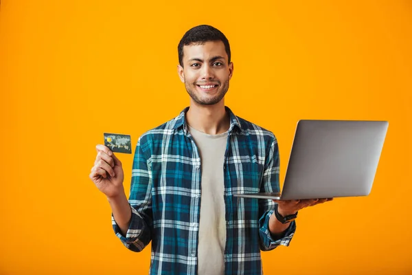 젊은이 오렌지 셔츠를 플라스틱 카드를 보여주는 노트북 컴퓨터를 — 스톡 사진