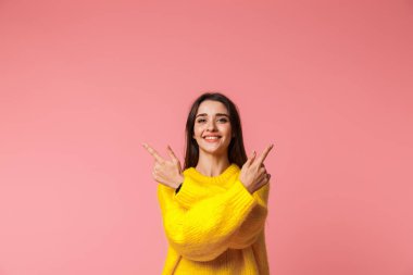 Parmakları her iki yönde işaret pembe arka plan üzerinde izole ayakta kazak giyen neşeli genç kız