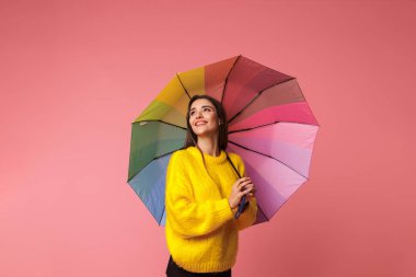 Pembe arka plan üzerinde izole bir şemsiye tutan kazak giyen neşeli genç kadın