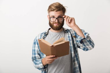 Yakışıklı bir genç sakallı adam kitap okuma holding beyaz duvar arka plan üzerinde izole ayakta görüntüsünü.