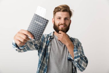 Yakışıklı bir genç sakallı adam pasaport holding beyaz duvar arka plan üzerinde izole ayakta görüntüsünü.