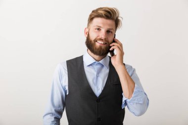 Yakışıklı bir genç sakallı adam cep telefonuyla konuşan beyaz duvar arka plan üzerinde izole ayakta resmini.
