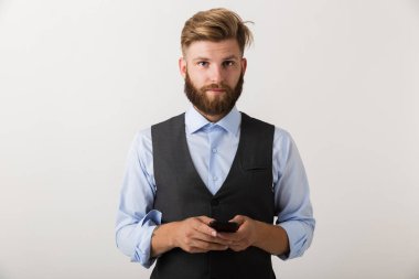 Yakışıklı bir genç sakallı adam cep telefonuyla beyaz duvar arka plan üzerinde izole ayakta fotoğrafı.