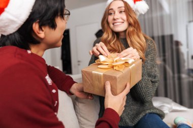 Fotoğraf süre kutlama yeni yıl hediye kutusu ile oturma odasında kanepede oturan mutlu çok ırklı çift