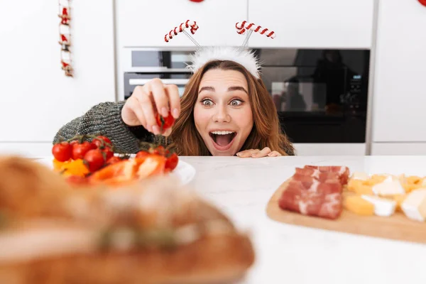 Fată Încântată Sărbătorește Crăciunul Poartă Coarne Reni Mănâncă Mâncare Masă — Fotografie, imagine de stoc