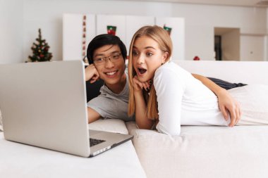 Görüntü çok ırklı çift erkek ve kadın yan yana gümüş laptop ile evde yatakta yatarken