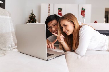 Görüntü neşeli çift erkek ve kadın yan yana gümüş laptop ile evde yatakta yatarken