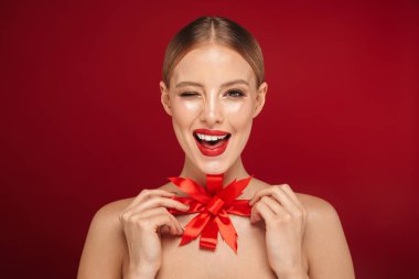 Noel yay tutan izole kırmızı arka plan üzerinde duran bir genç ve güzel üstsüz kadın güzellik portresi