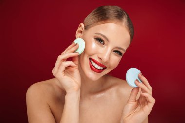 Pamuk tamponlarla tutan izole kırmızı arka plan üzerinde duran bir genç ve güzel üstsüz kadın güzellik portresi