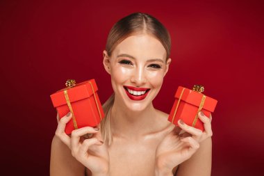 İki küçük hediye kutuları gösterilen kırmızı arka plan üzerinde izole makyaj oldukça genç bir üstsüz kadın güzellik portresi