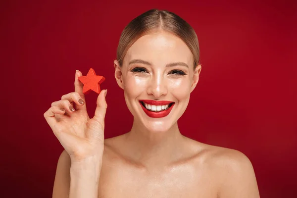 Beauty portrait of a pretty young topless woman standing isolated over red background, holding Christmas cookies