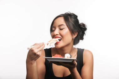 Beyaz arka plan üzerinde izole bir plaka suşi yemek masasında oturan oldukça mutlu Asyalı kadın