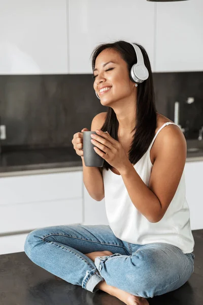 Photo Young Asian Woman Wearing Headphones Holding Cup While Sitting — Stock Photo, Image