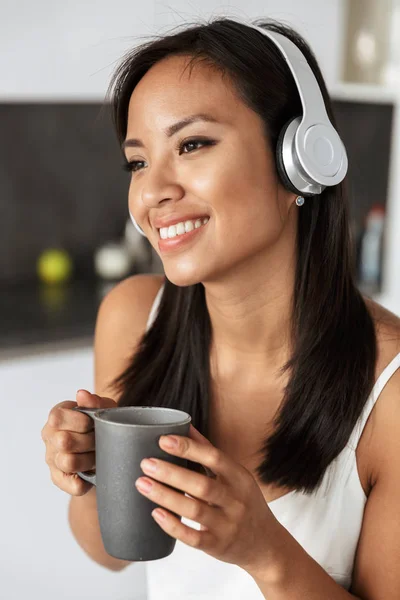 Photo Attractive Asian Woman Wearing Headphones Holding Cup While Sitting — Stock Photo, Image