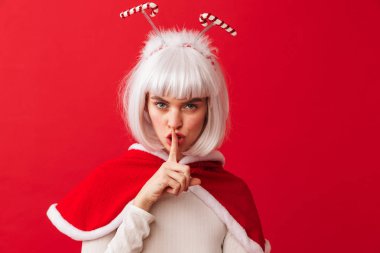 Sessizlik jest gösterilen kırmızı arka plan üzerinde izole duran kırmızı yılbaşı kostüm giyen güzel genç kız