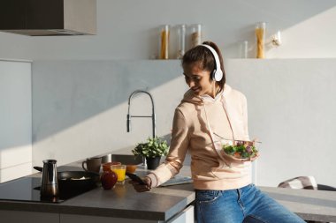 Salata bir kase yemek neşeli genç kız evde mutfak at kulaklık ile müzik dinlemek