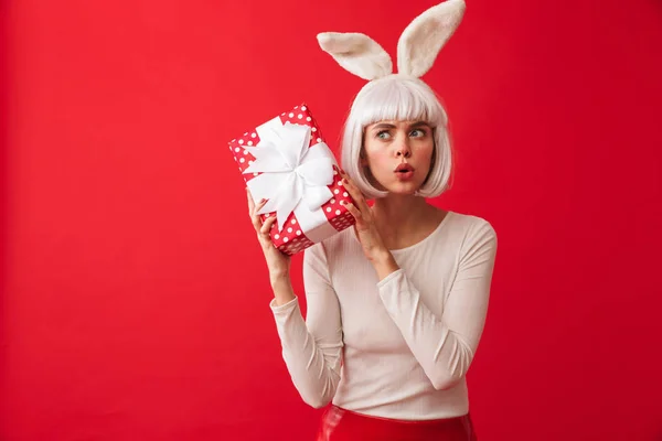 ギフトを押し赤い壁背景に分離ポーズ カーニバル クリスマス衣装を着て興奮して若いショックを受けた女性のイメージ — ストック写真