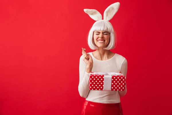 愉快的年轻女孩戴着圣诞兔子耳朵站在孤立的红色背景 拿着礼品盒 — 图库照片