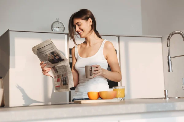 早上微笑着站在厨房里的年轻女孩 看报纸 — 图库照片